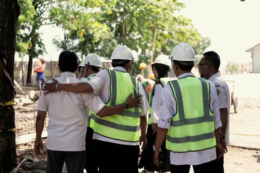 Equipo de trabajadores con chalecos de alta visibilidad y cascos, abrazados de espaldas en una obra