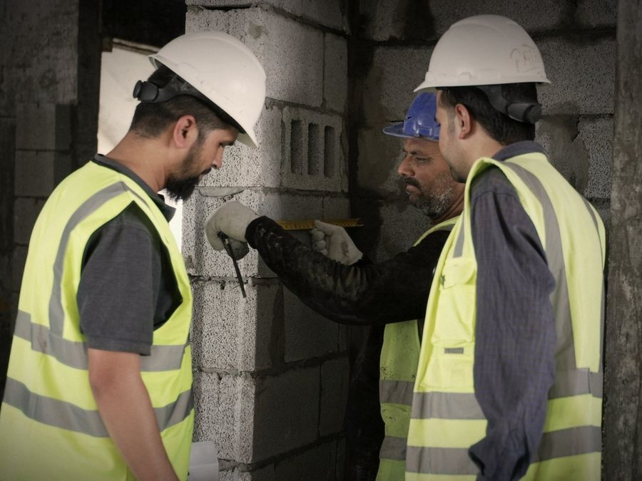 Dos inspectores con casco y chaleco examinan de cerca un muro de bloques