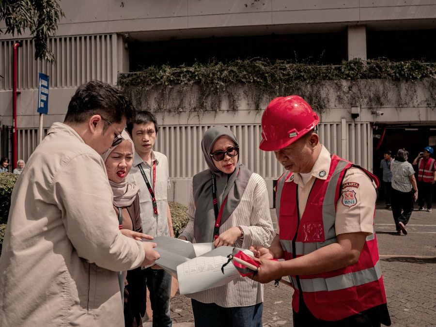 Brigadista con casco rojo revisa un documento junto a un grupo de personas en el exterior de un edificio